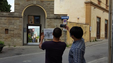 Two students face a building and take photos.