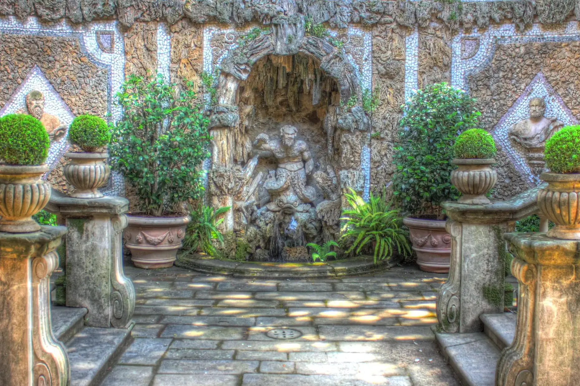Fountain with the Greek god Triton at it's center, flanked by monumental staircases and several potted green plants.