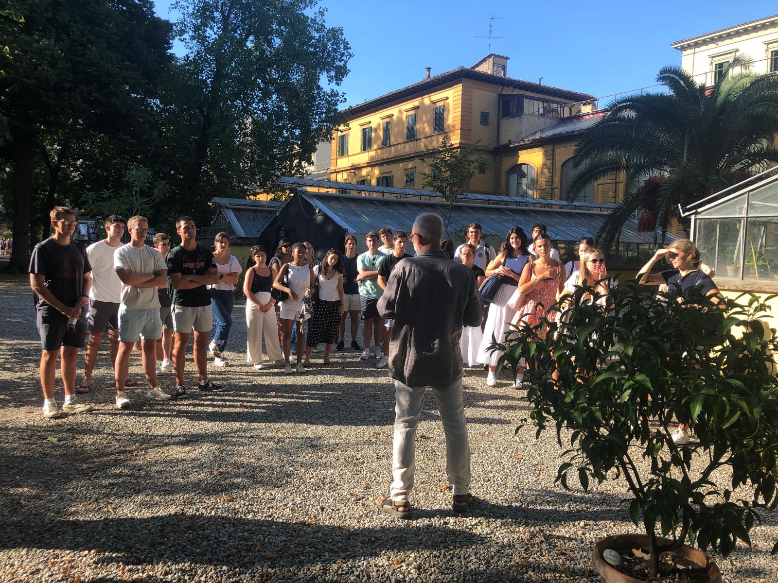 A large group of students in an outdoor setting standing in front of a man with his back to the camera.