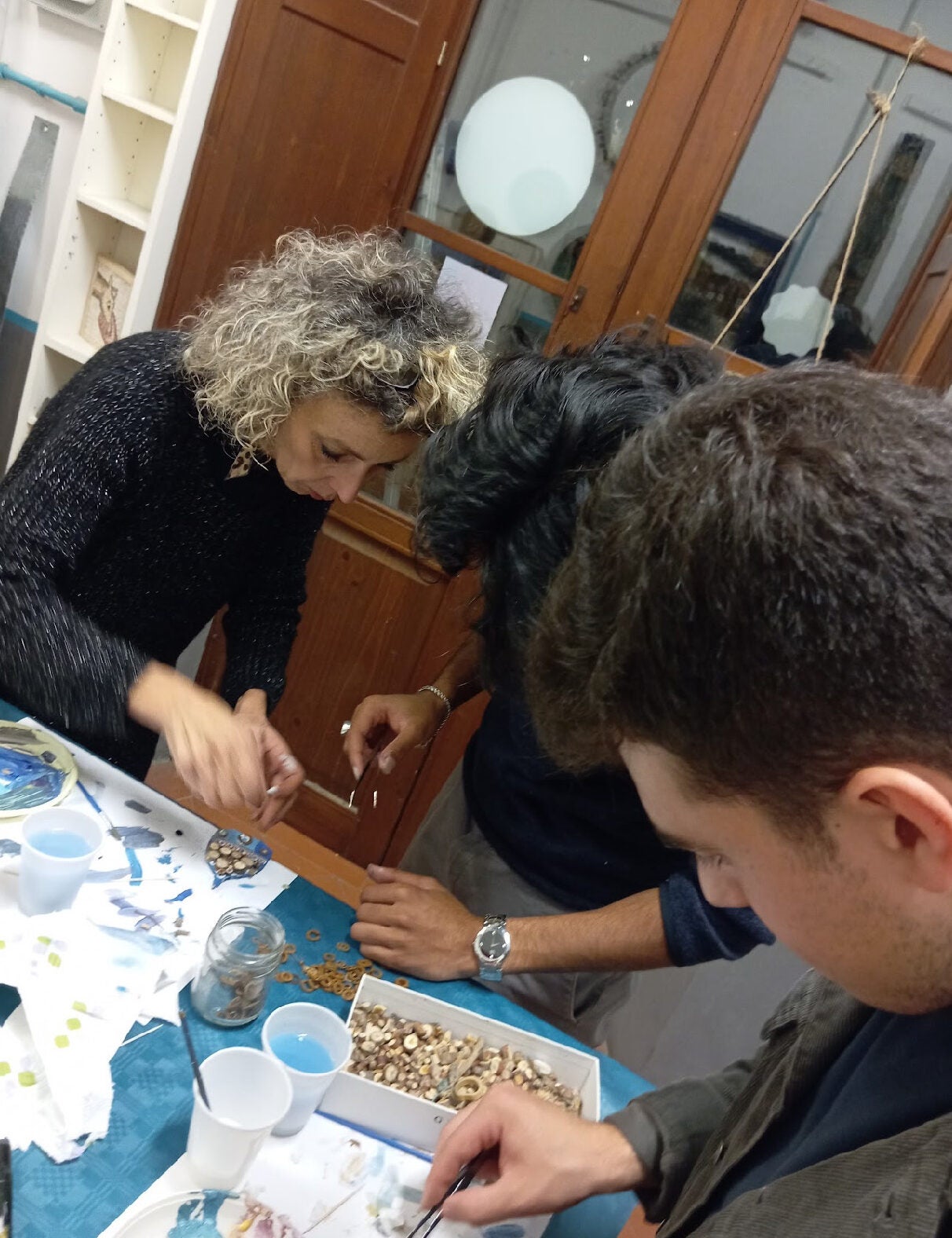 Three people with their heads bent over a table placing small pieces of glass on a shape.