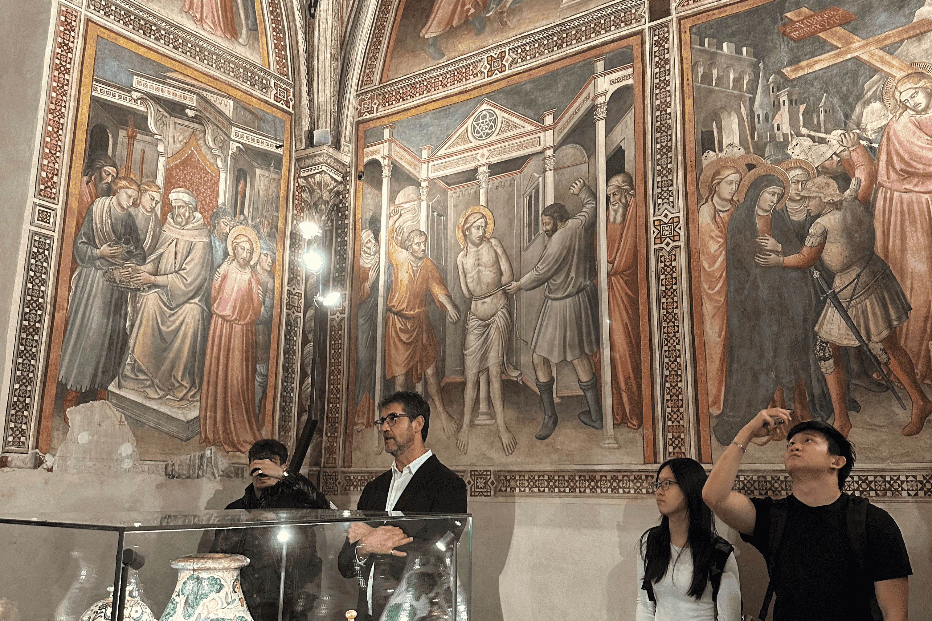 Four individuals standing in a room of the Officina with detailed religious murals.